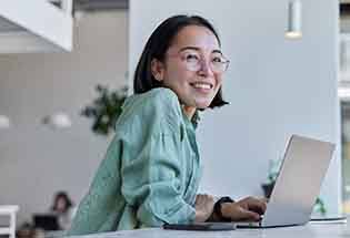 Woman with glasses smile at desk with laptop