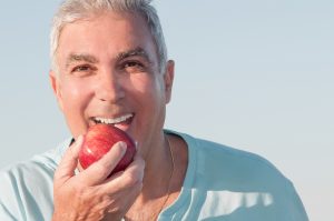 older smiling holding red apple